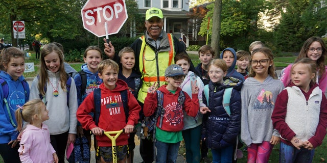 Alec Childress, 80, poses with school children he helps as a crossing guard in Illinois. On Thursday, his birthday, they surprised him with a big celebration to thank him for brightening their day every morning.