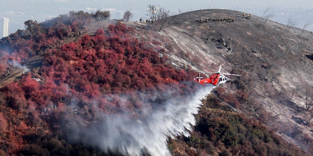 A helicopter drops water as a wildfire called the Getty fire burns on Kenter Canyon in Los Angeles, Monday, Oct. 28, 2019.