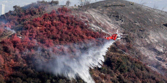 A helicopter drops water as a wildfire called the Getty fire burns on Kenter Canyon in Los Angeles, Monday, Oct. 28, 2019.