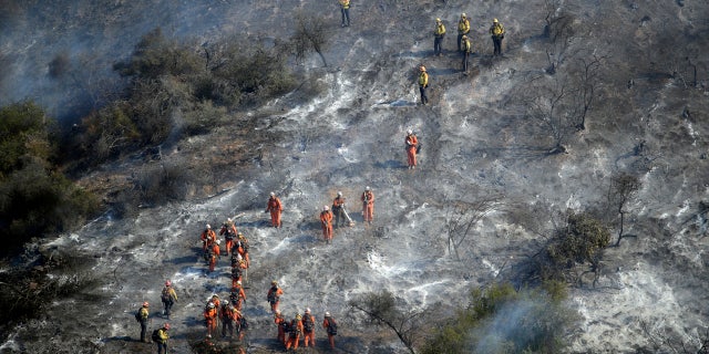 Hand crews work a wildfire-damaged hillside as the Getty fire burns on Mandeville Canyon, Oct. 28, 2019, in Los Angeles.