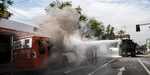 A police water cannon extinguishes a burning bus that was set alight by demonstrators during a protest in Santiago, Chile, Saturday, Oct. 19, 2019.