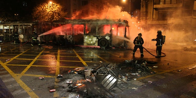 Firefighters put out the flames on a burning bus during a protest against the rising cost of subway and bus fares, in Santiago, Friday, Oct. 18, 2019.