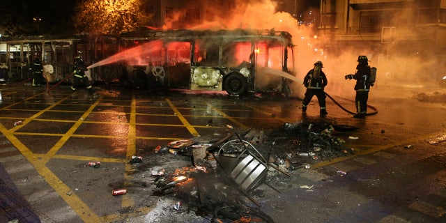 Firefighters put out the flames on a burning bus during a protest against the rising cost of subway and bus fares, in Santiago, Friday, Oct. 18, 2019.