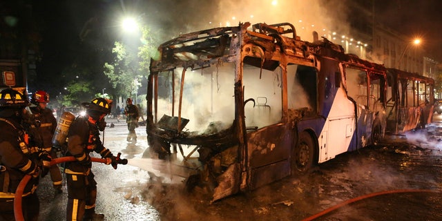 Firefighters put out the flames on a burning bus during a protest against the rising cost of subway and bus fares, in Santiago, Friday, Oct. 18, 2019.