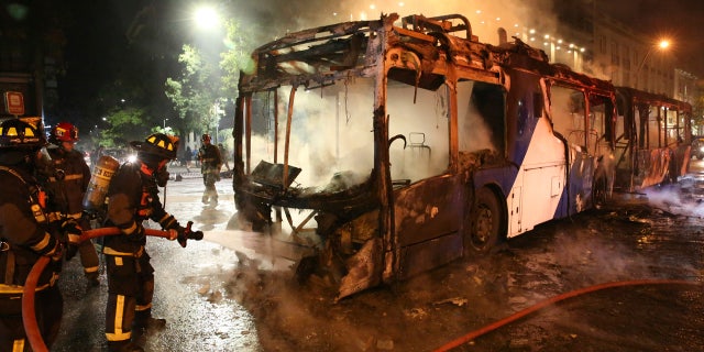 Firefighters put out the flames on a burning bus during a protest against the rising cost of subway and bus fares, in Santiago, Friday, Oct. 18, 2019.
