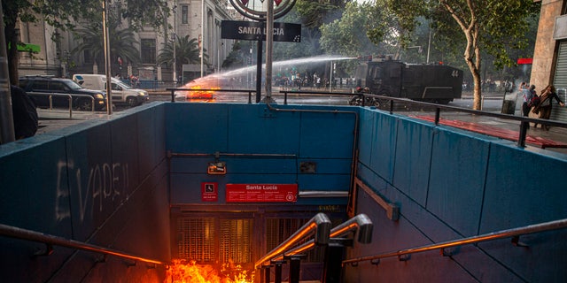 A police water cannon puts out a burning barricade near the Santa Lucia subway station during a protest against the rising cost of subway and bus fares, in Santiago, Friday, Oct. 18, 2019.