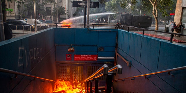 A police water cannon puts out a burning barricade near the Santa Lucia subway station during a protest against the rising cost of subway and bus fares, in Santiago, Friday, Oct. 18, 2019.