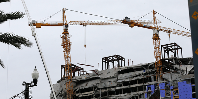 Two unstable cranes loom over the construction of a Hard Rock Hotel, Thursday, Oct. 17, 2019, in New Orleans. The 18-story hotel project that was under construction collapsed last Saturday, killing three workers. Two bodies remain in the wreckage. Authorities say explosives will be strategically placed on the two unstable construction cranes in hopes of bringing them down with a series of small controlled blasts ahead of approaching tropical weather. (AP Photo/Gerald Herbert)