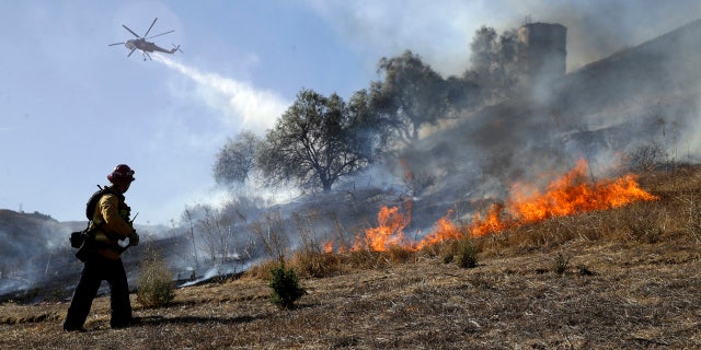 Trinh Nguyen, of the Camarillo Fire Dept, monitors the advance of the Easy Fire as a helicopter makes a water drop Wednesday, Oct. 30, 2019, in Simi Valley, Calif.