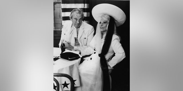 American actors John Huston and Mae West sit at a restaurant table in a still from the film