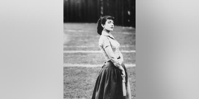 Portrait of Greek-American opera singer Maria Callas (1923 - 1977), standing outdoors in a field and holding a hand fan, Rome, Italy.