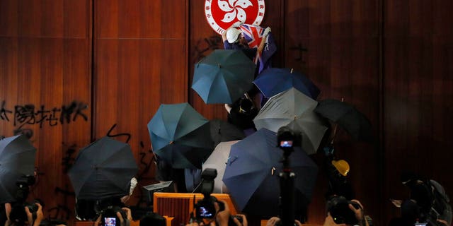 FILE - In this July 1, 2019, file photo, a protester covers the Hong Kong emblem with a Hong Kong colonial flag after they broke into the Legislative Council building in Hong Kong. Hong Kong authorities on Wednesday, Oct. 23, 2019 withdrew an unpopular extradition bill that sparked months of chaotic protests that have since morphed into a campaign for greater democratic change. (AP Photo/Kin Cheung, File)