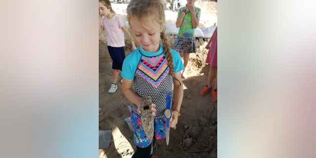 A young excavator holds the iron hammer that was discovered in the Usha excavation.