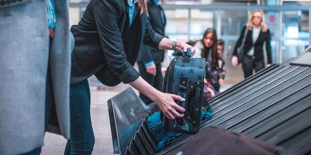 A woman is shown picking up her luggage from a conveyor belt at an airport terminal — something that hundreds of passengers are claiming they have been unable to do at one airport. 