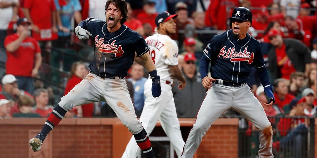 Atlanta Braves' Dansby Swanson, left, and Rafael Ortega, right, celebrate after scoring as St. Louis Cardinals relief pitcher Carlos Martinez (18) walks in the background during the ninth inning in Game 3 of a baseball National League Division Series on Sunday, Oct. 6, 2019, in St. Louis. (AP Photo/Jeff Roberson)