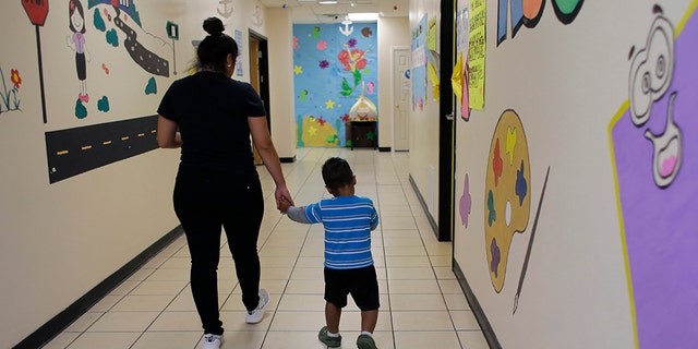 A young migrant boy walks with a Comprehensive Health Services caregiver at a "tender-age" facility for babies, children and teens, in Texas' Rio Grande Valley, Thursday, Aug. 29, 2019, in San Benito, Texas. Sheltering migrant children has become a booming business for Comprehensive Health Services, a Florida-based government contractor, as the number of children in government custody has swollen to record levels over the past two years. (AP Photo/Eric Gay)
