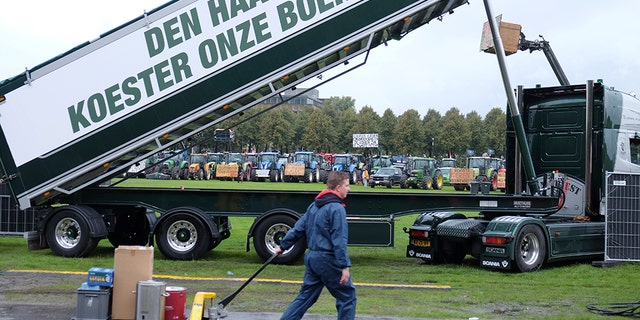 A worker walks past a truck with a banner saying: "The Hague: Cherish our farmers!", refrying to the government, as tractors driven by protesting farmers line up in the background during a protest in The Hague, Netherlands, Tuesday, Oct. 1, 2019. (AP Photo/Mike Corder)