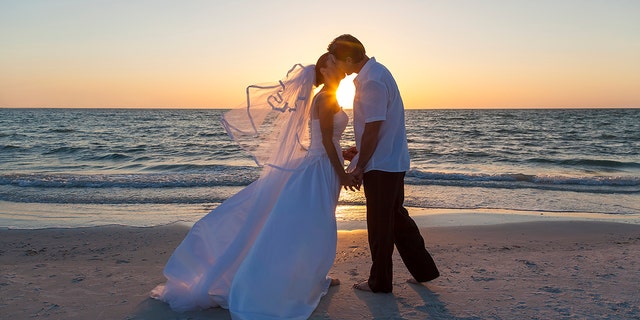 A married couple, bride and groom, kissing at sunset or sunrise on a beautiful tropical beach (Photo: iStock)