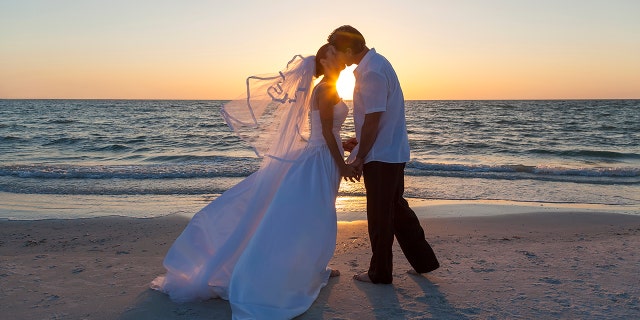 A married couple, bride and groom, kissing at sunset or sunrise on a beautiful tropical beach (Photo: iStock)
