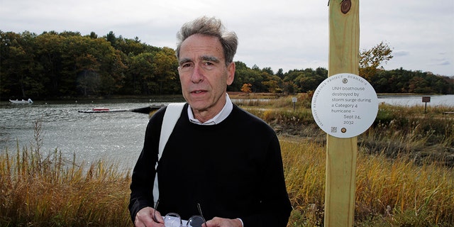 Artist Thomas Starr posing next to a sign on the banks of the Oyster River in Durham, N.H., last week. (AP Photo/Charles Krupa)