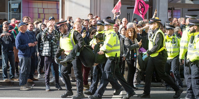 Police arrest an activist as hundreds of members of the Extinction Rebellion environmental activist group swarm Oxford circus with three activists erecting a road blocking wooden pyramid structure with an upside down tree hanging in the middle on October 18, 2019 in London, England.