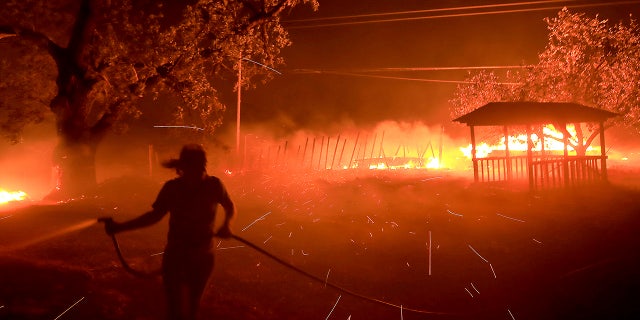 Susi Weaver, the manager for the Hawkeye Ranch in the Mayacamas Mountains above Geyserville, Calif., sprays down the dry brush as the Kincade fire delivers firebrands across the property, Thursday, Oct. 24, 2019.