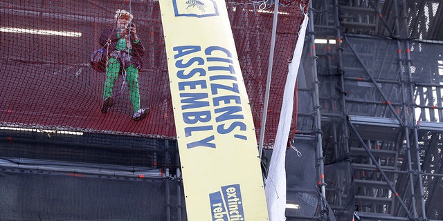 A climate protester demonstrates with banners on the scaffolding covering the Elizabeth Tower that houses the Big Ben clock in London, Friday, Oct. 18, 2019.