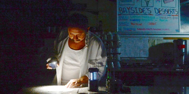 Carlos Lama of Bayside Cafe, which was among businesses to lose power due to PG&E's public safety power shutoff, uses an LED lamp and light from his phone at the counter of the restaurant in Sausalito, Calif. (Alan Dep/Marin Independent Journal via AP)