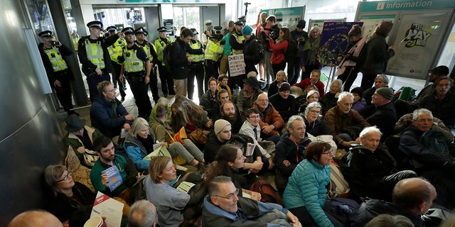Police Officers stand guard as Extinction Rebellion demonstrators peacefully block an entrance to City Airport in London, Thursday, Oct. 10, 2019. Some hundreds of climate change activists are in London during a fourth day of world protests by the Extinction Rebellion movement to demand more urgent actions to counter global warming. (AP Photo/Matt Dunham)