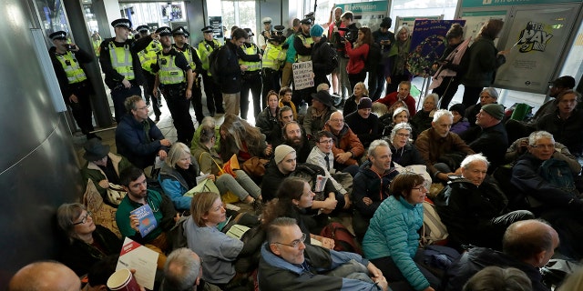 Police Officers stand guard as Extinction Rebellion demonstrators peacefully block an entrance to City Airport in London, Thursday, Oct. 10, 2019. Some hundreds of climate change activists are in London during a fourth day of world protests by the Extinction Rebellion movement to demand more urgent actions to counter global warming. (AP Photo/Matt Dunham)