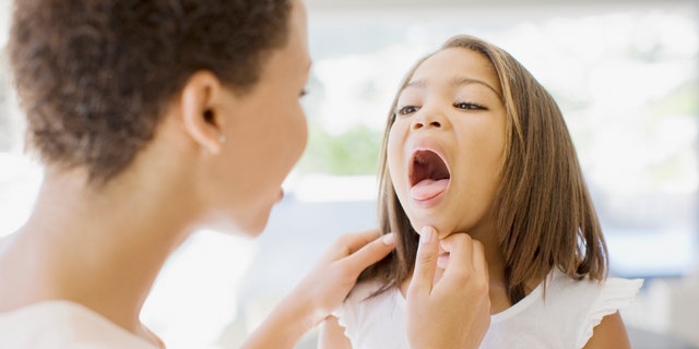 A mom checks her sick daughter's throat. 