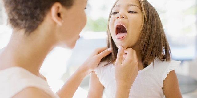 A mom checks her sick daughter's throat. 