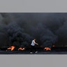 A woman walks by burning tires that were set fire to block a road during a protest against the government's plans to impose new taxes in Beirut, Lebanon, Oct. 18, 2019. 