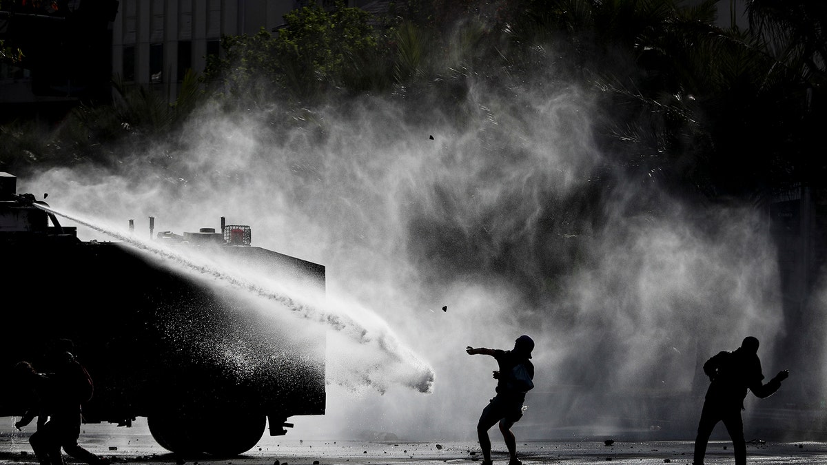 Demonstrators clash with a police water cannon during an anti-government protest in Santiago, Tuesday, Nov. 5, 2019. Chileans have been taking to the streets and clashing with the police to demand better social services and an end to economic inequality, even as the government announced that weeks of demonstrations are hurting the country's economic growth. (AP Photo/Esteban Felix)