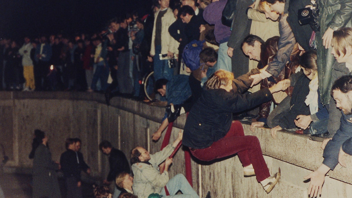 People climbing the Berlin Wall which had divided the city since the end of World War II, near the Brandenburg Gate, on Nov. 10, 1989. (AP Photo/Jockel Finck, File)