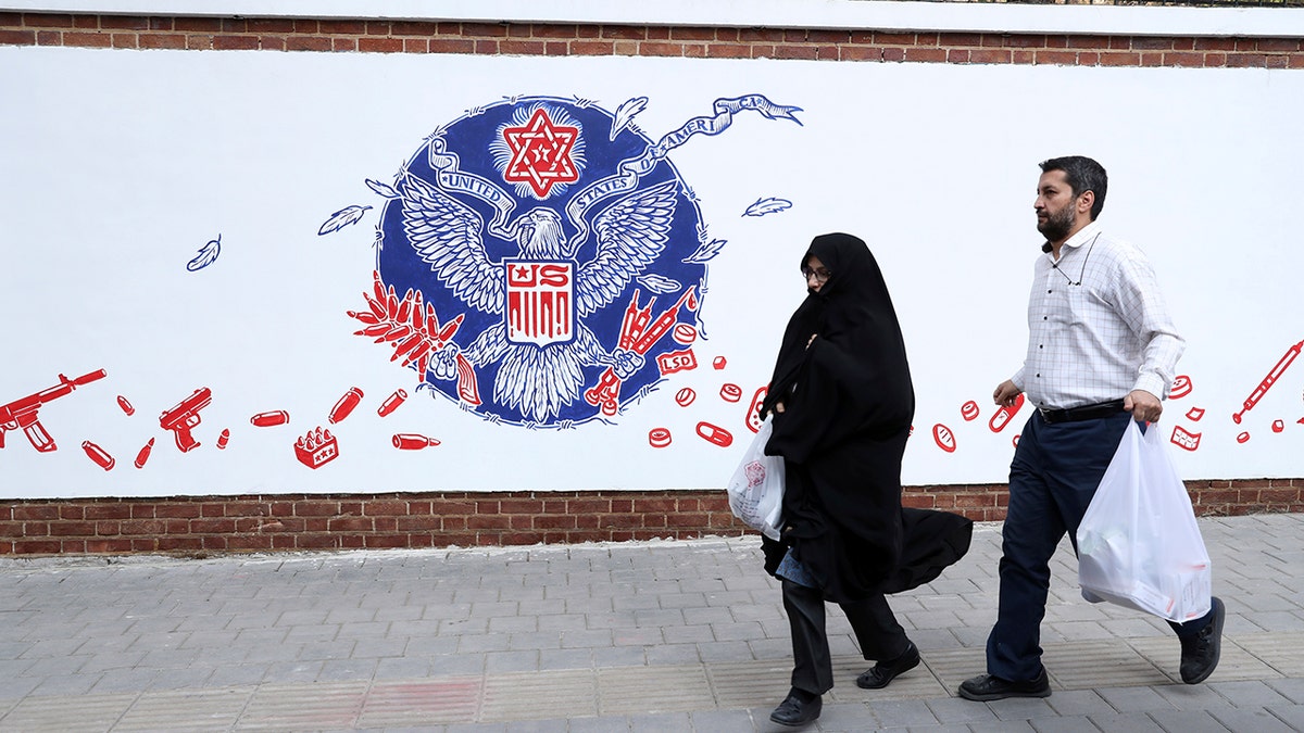 People walk past a satirical drawing of the Great Seal of the United States after new anti-U.S. murals on the walls of former U.S. embassy unveiled in a ceremony in Tehran, Iran, Saturday, Nov. 2, 2019. (AP Photo/Vahid Salemi)