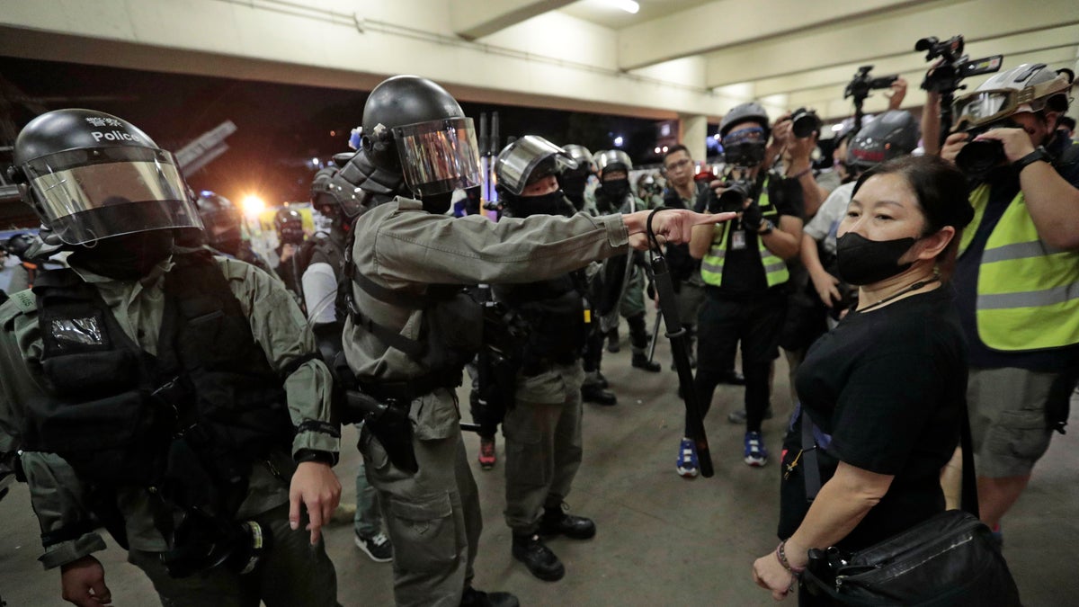 Police in riot gear ask a woman to take off her mask outside a train station in Hong Kong, Sunday, Nov. 3, 2019. Riot police stormed several malls in Hong Kong on Sunday in a move to thwart more pro-democracy protests, as the city's leader heads to Beijing for talks on deepening economic integration between the semi-autonomous Chinese territory and mainland China. (AP Photo/Dita Alangkara)