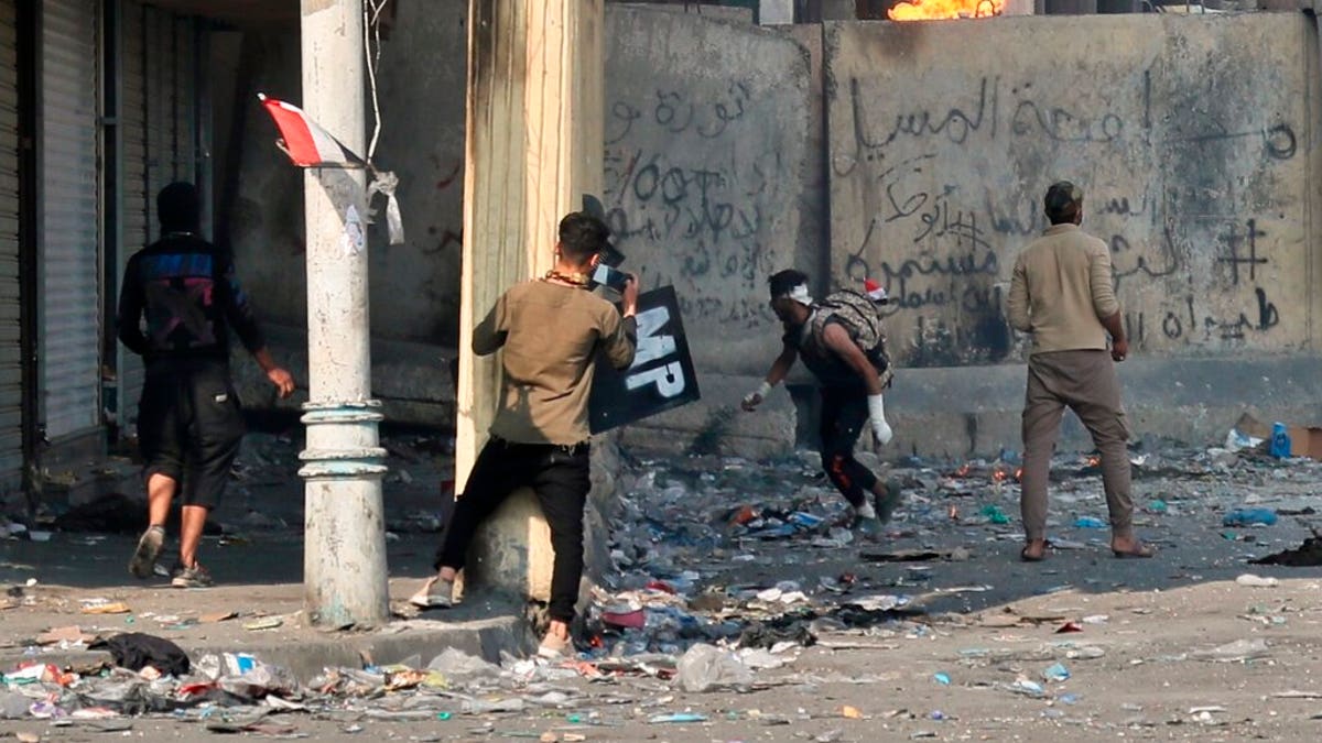 Anti-government protesters throw a Molotov cocktail toward riot police during clashes in Baghdad. 