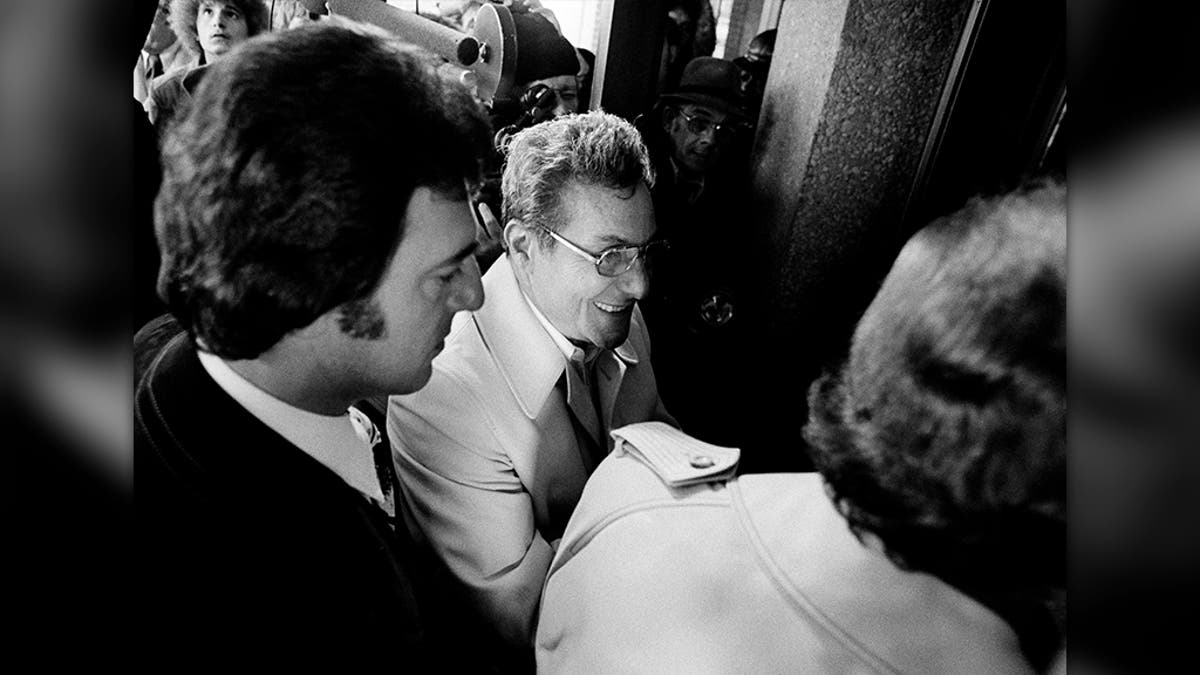Salvatore Briguglio, center, smiles as he waits to enter the lobby of the Oakland County Jail in Pontiac, Mich., Dec. 6, 1975 where he was to appear in a court ordered lineup in connection with the disappearance of James R. Hoffa. Thomas Andretta, left, was also to appear in the lineup. (AP Photo)