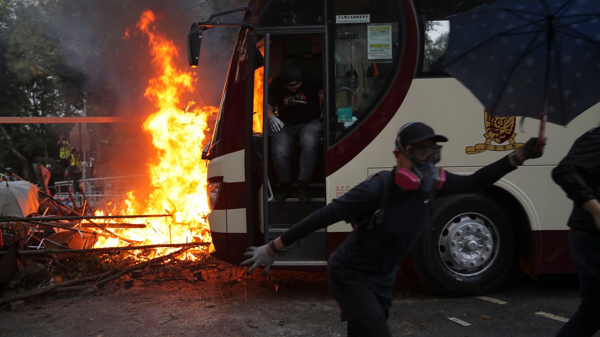 Students run past fire set near a bus during a face-off with riot police at the Chinese University in Hong Kong, Tuesday, Nov. 12, 2019.