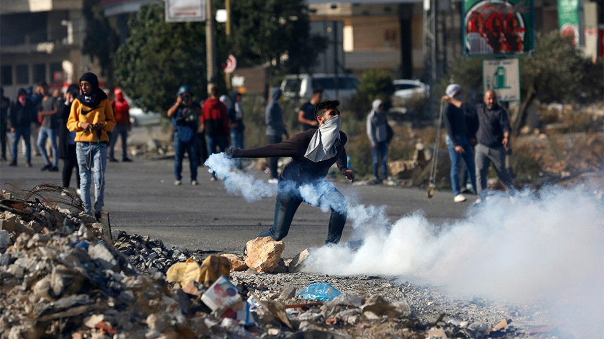 Palestinian demonstrator throws back tear gas fired by Israeli troops during the protest against the U.S. announcement that it no longer believes Israeli settlements violate international law., at checkpoint Beit El near the West Bank city of Ramallah, Tuesday, Nov. 26, 2019.