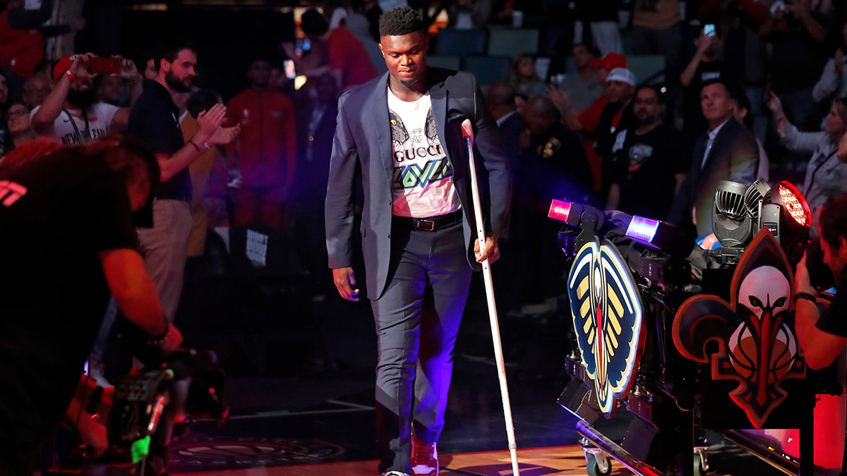 New Orleans Pelicans forward Zion Williamson walk onto the court with a crutch as he is introduced before an NBA basketball home-opener game against the Dallas Mavericks in New Orleans, Friday, Oct. 25, 2019. (AP Photo/Gerald Herbert)