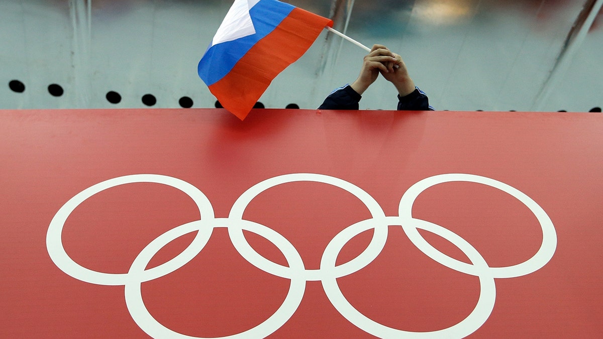 FILE - In this Feb. 18, 2014, file photo, a Russian flag is held above the Olympic Rings at Adler Arena Skating Center during the Winter Olympics in Sochi, Russia. A World Anti-Doping Agency (WADA) panel on Monday Nov. 25, 2019, has recommended Russian athletes be forced to compete as neutrals at the 2020 Olympics in Tokyo and other major upcoming events. (AP Photo/David J. Phillip, File)