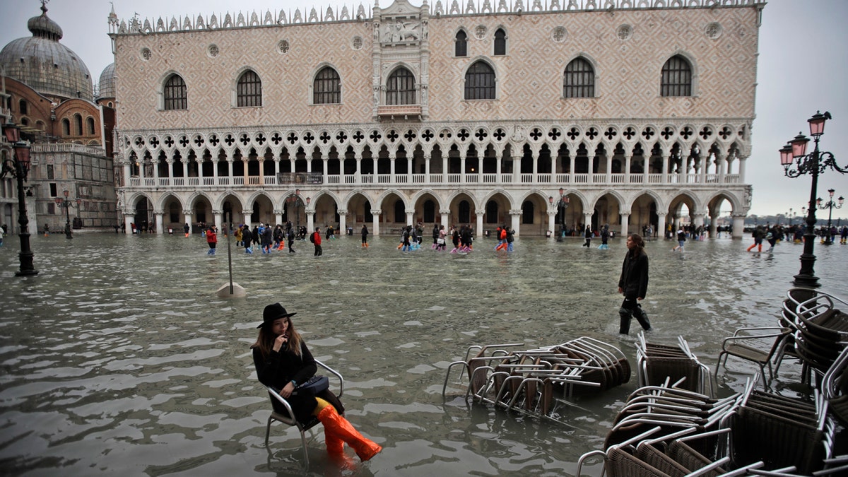 A woman sits in a chair in a flooded St. Mark's Square, in Venice, Wednesday, Nov. 13, 2019.
