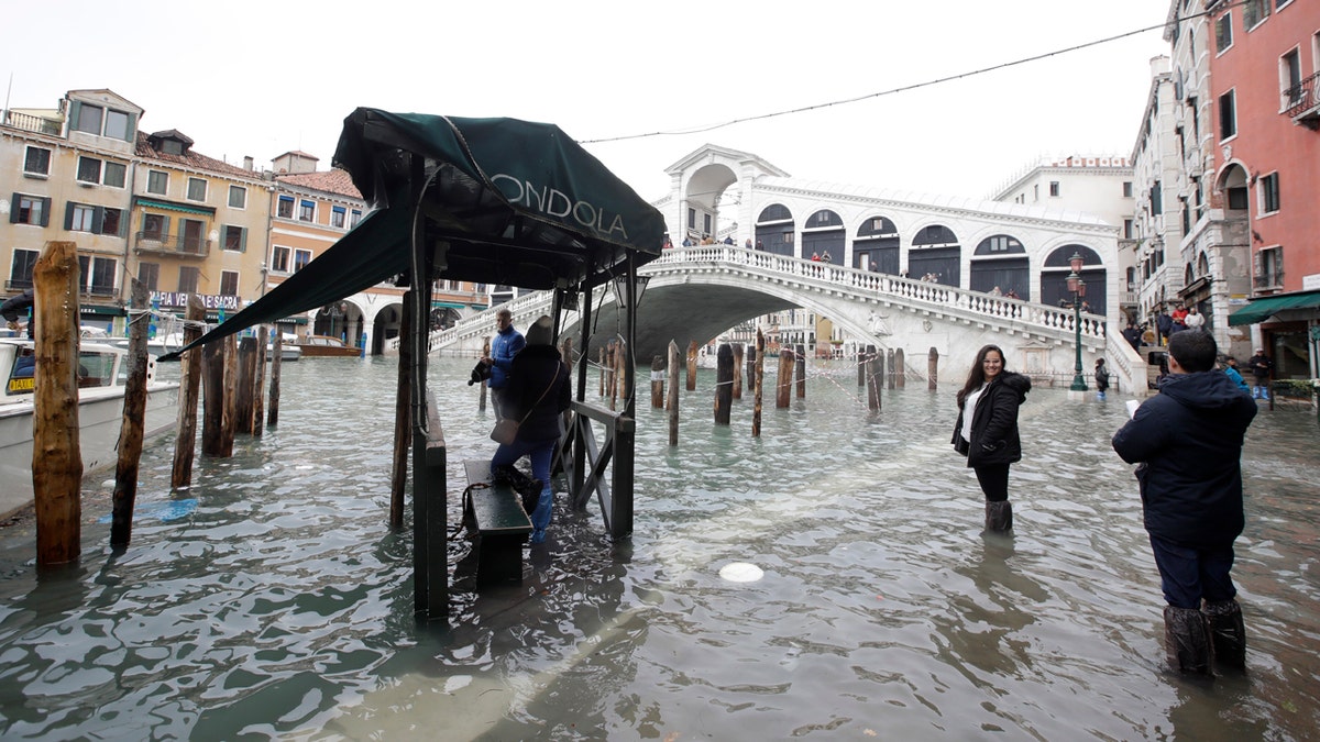 Tourists take pictures in front of the Rialto Bridge while wading through high water, in Venice, Wednesday, Nov. 13, 2019.