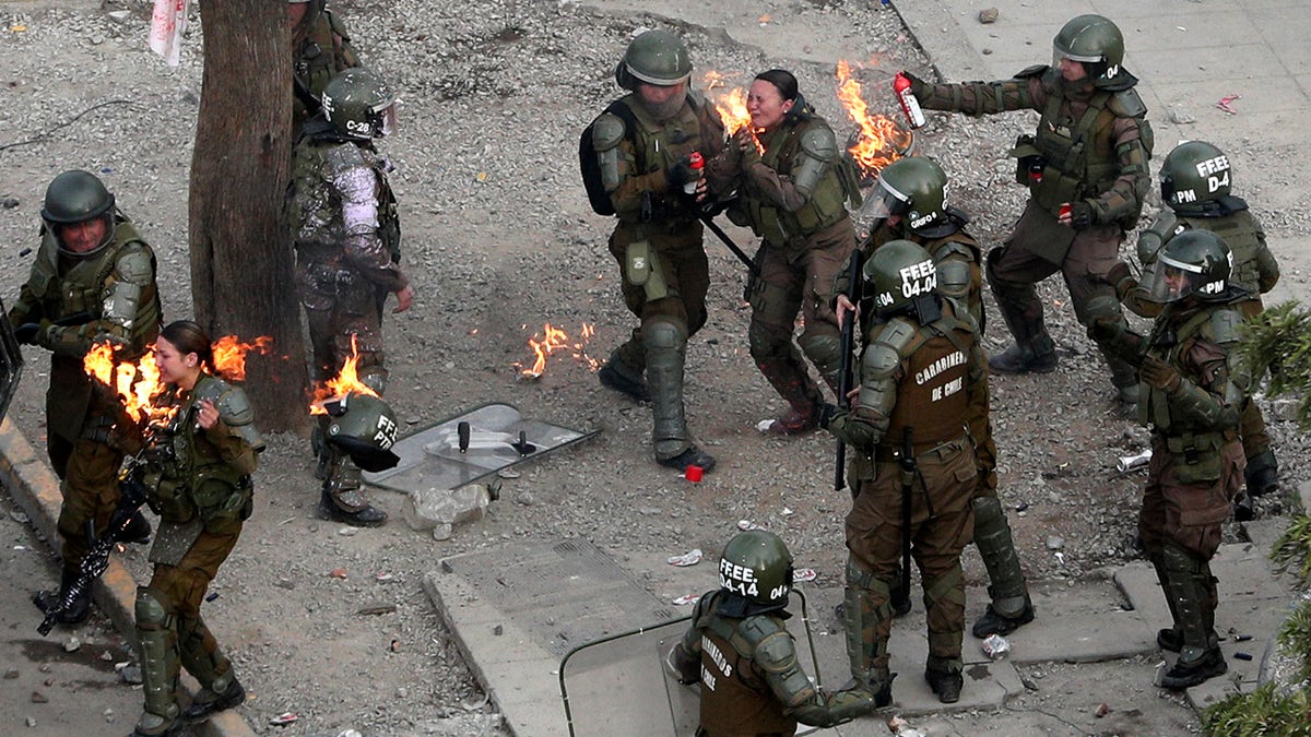 Police officers run to get assistance after being hit with a gasoline bomb thrown by protesters during an anti-government protest in Santiago, Chile, Monday, Nov. 4, 2019.