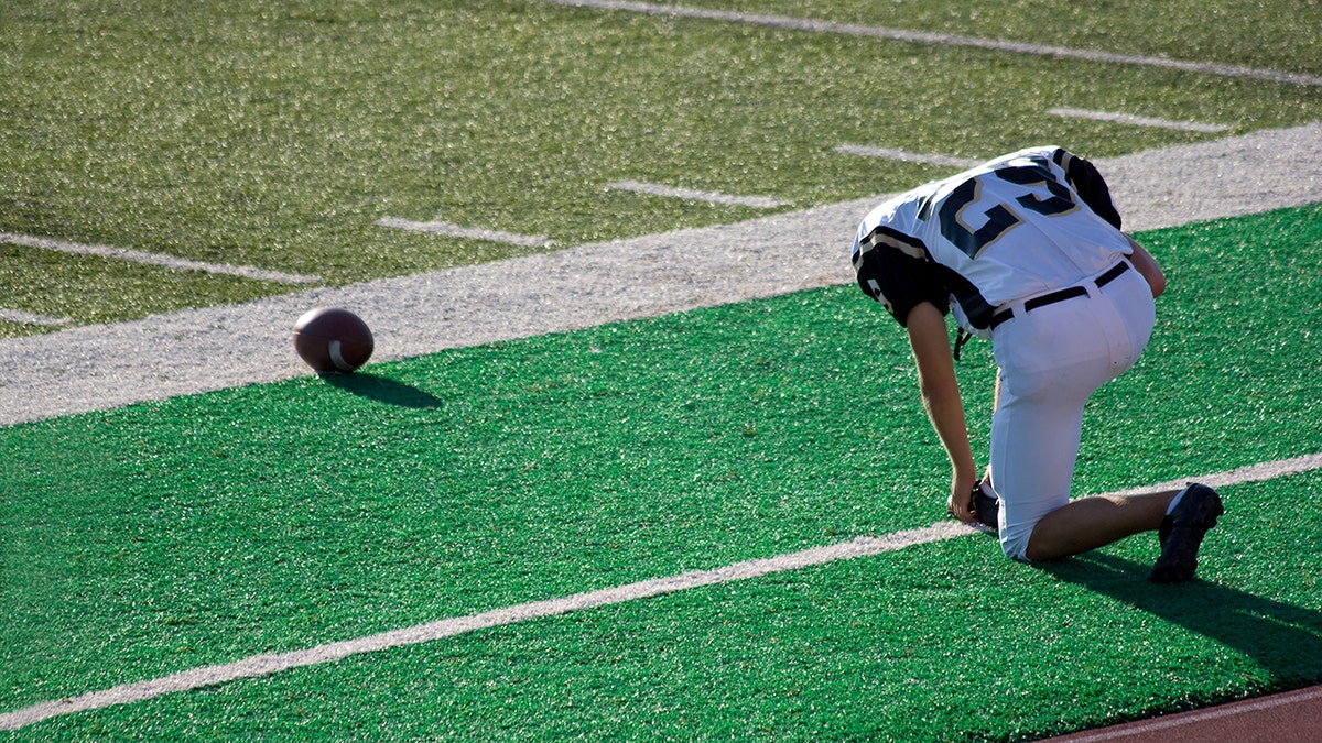 "Football player prays on the sidelines before a game. Color space is ProPhoto, RGB, processed from a 16 bit RAW image.