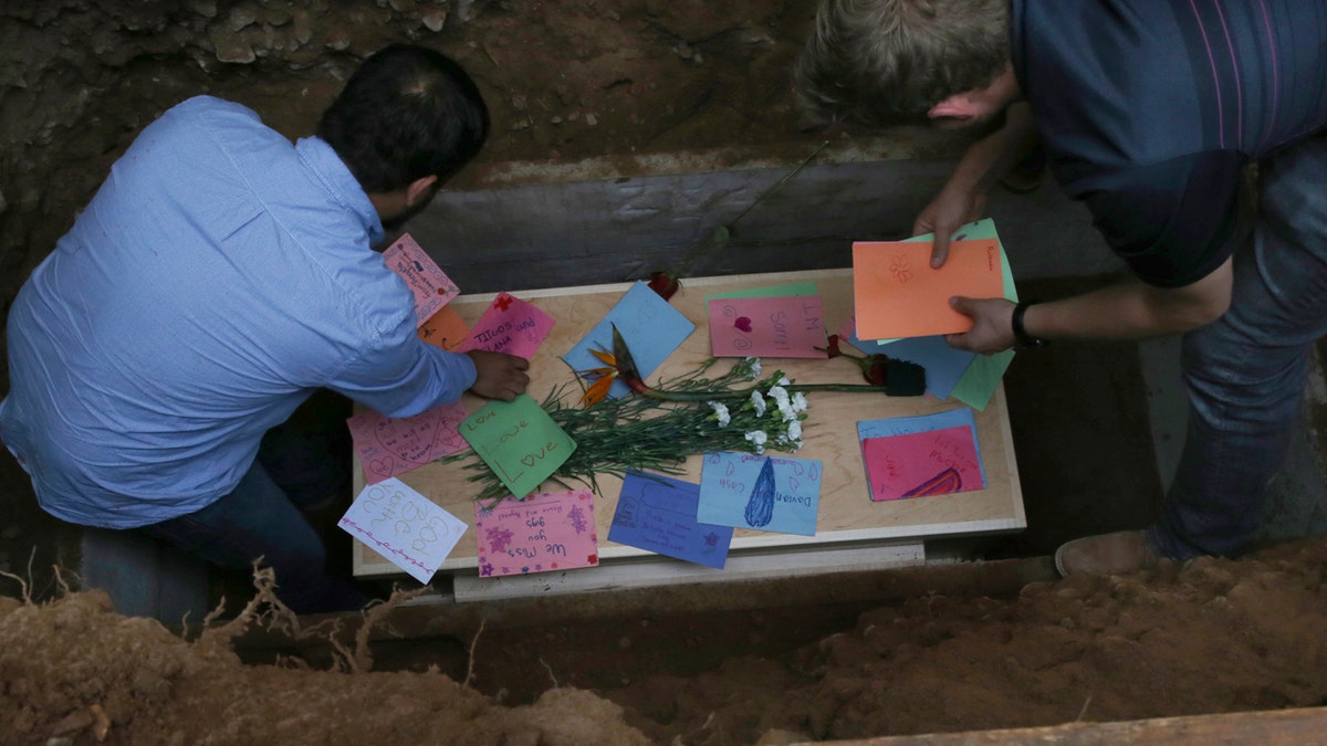 Men arrange personal notes on the coffin that contains the remains of 12-year-old Howard Jacob Miller Jr., at the cemetery in Colonia Le Baron, Mexico, Friday, Nov. 8, 2019, during a burial service for Rhonita Miller and four of her young children, who were murdered by drug cartel gunmen.(AP Photo/Marco Ugarte)