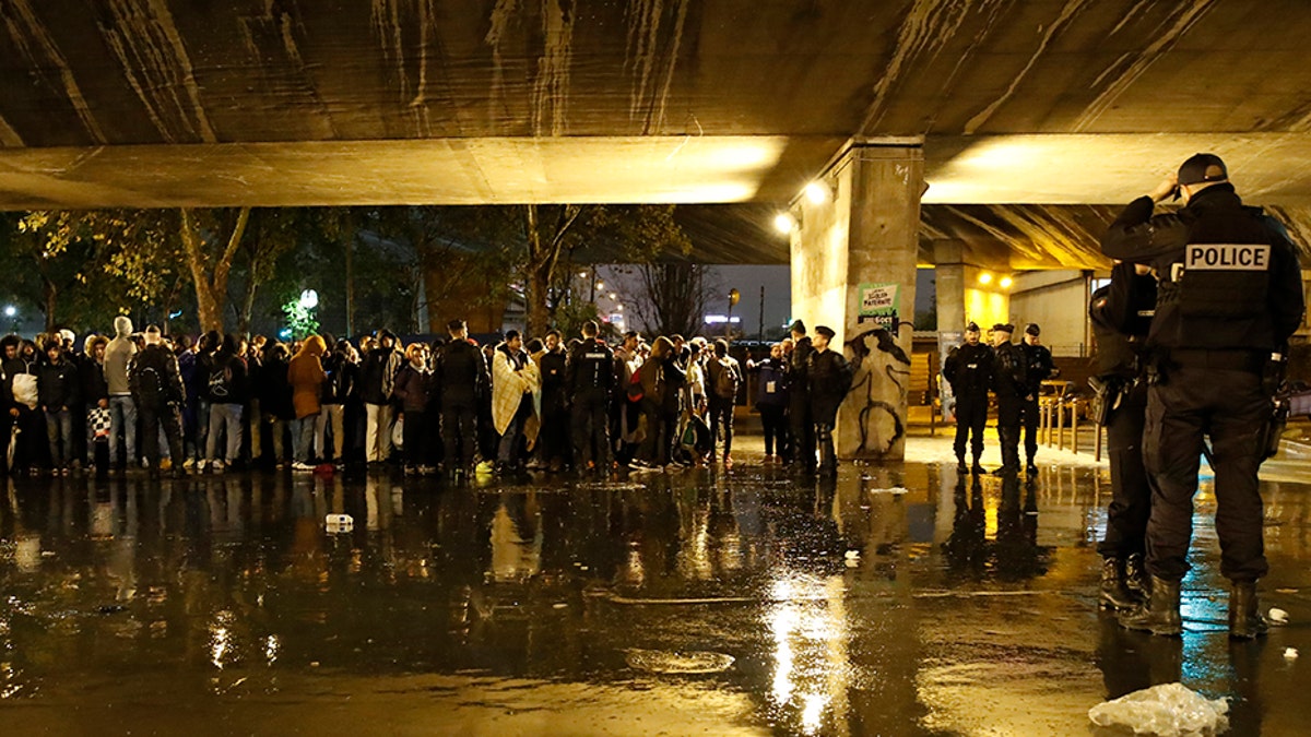 Police officers guard migrants as they clear a camp Thursday in northern Paris. (AP)