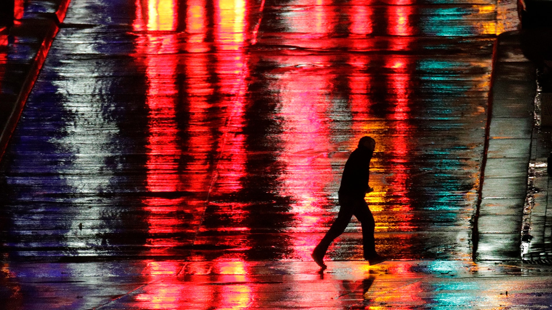 A man is silhouetted as he crosses a rain-covered street on a cold, windy night in Kansas City, Missouri, Nov. 26, 2019.